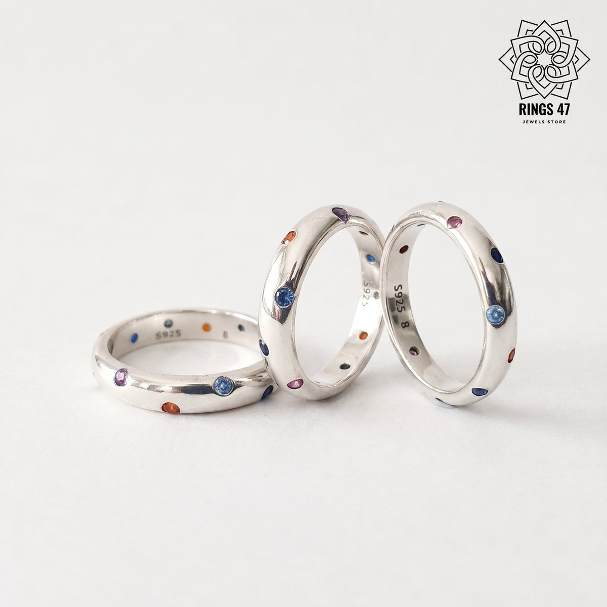Trois bagues en argent 925 ornées de zirconiums colorés, sur fond blanc