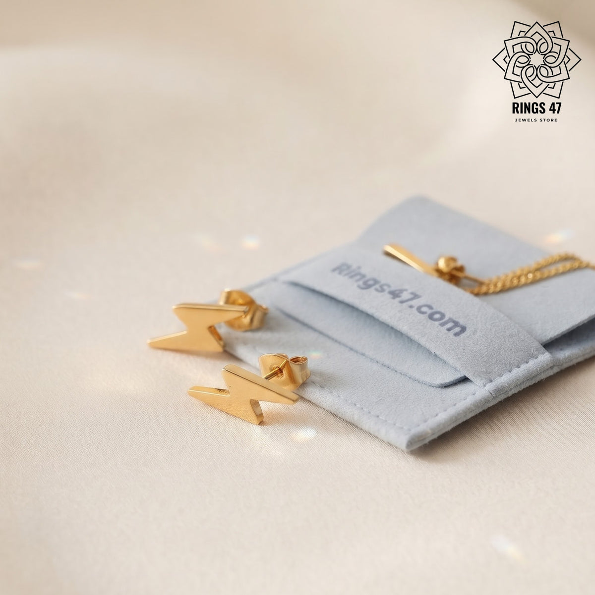 Boucle d'oreilles eclairs en acier inoxydable dorées sur fond blanc à coté du pochon Rings47