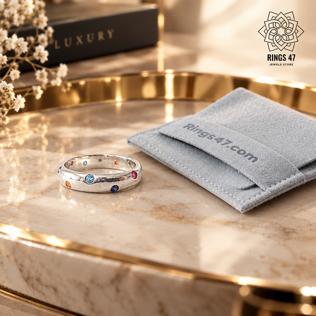 Bague en argent 925 aux zirconiums multicolores posée sur un plateau en marbre doré, avec une pochette Rings47